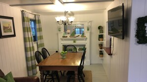 A dining area with a wooden table, chairs, a chandelier, and a TV mounted on the wall. - Charming lake front cabin on Highland Lake (Andover)