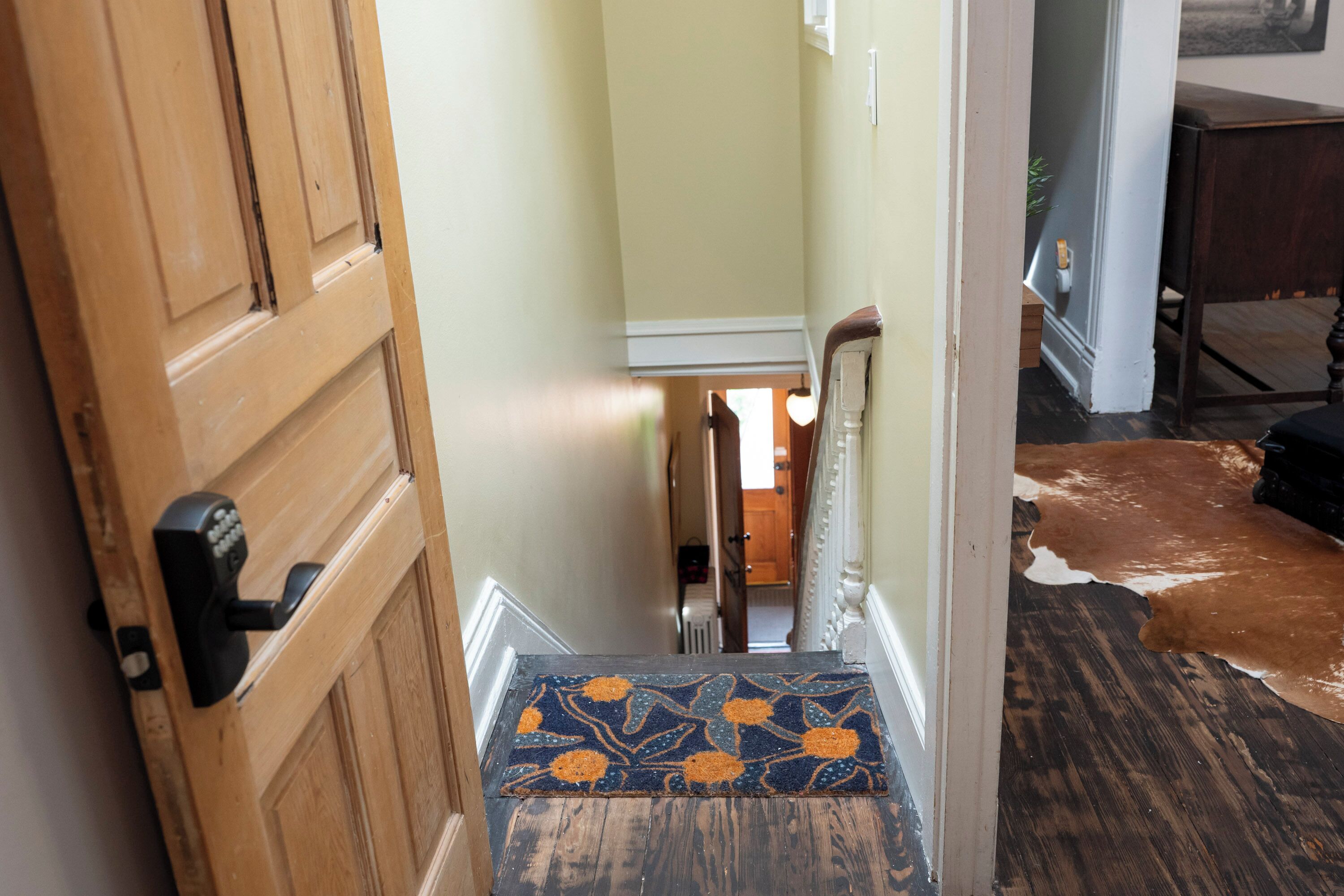A wooden door with a keypad lock, a carpeted staircase, and a cowhide rug on the floor.