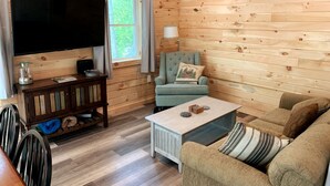 A cozy cabin interior with a wooden interior, a television, a sofa, and a chair. - Cozy Haven: A Lakeside Cottage Near Acadia (Orland)
