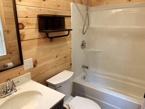 A bathroom with a wooden wall, a white sink, a toilet, and a bathtub. - Cozy Haven: A Lakeside Cottage Near Acadia (Orland)
