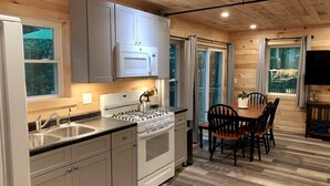 A modern kitchen with stainless steel appliances, wooden cabinets, and a dining area with a table and chairs. - Cozy Haven: A Lakeside Cottage Near Acadia (Orland)