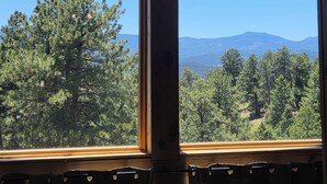 Ein Zimmer mit großem Fenster, Holzbalken und Blick auf einen bewaldeten Gebirgszug.