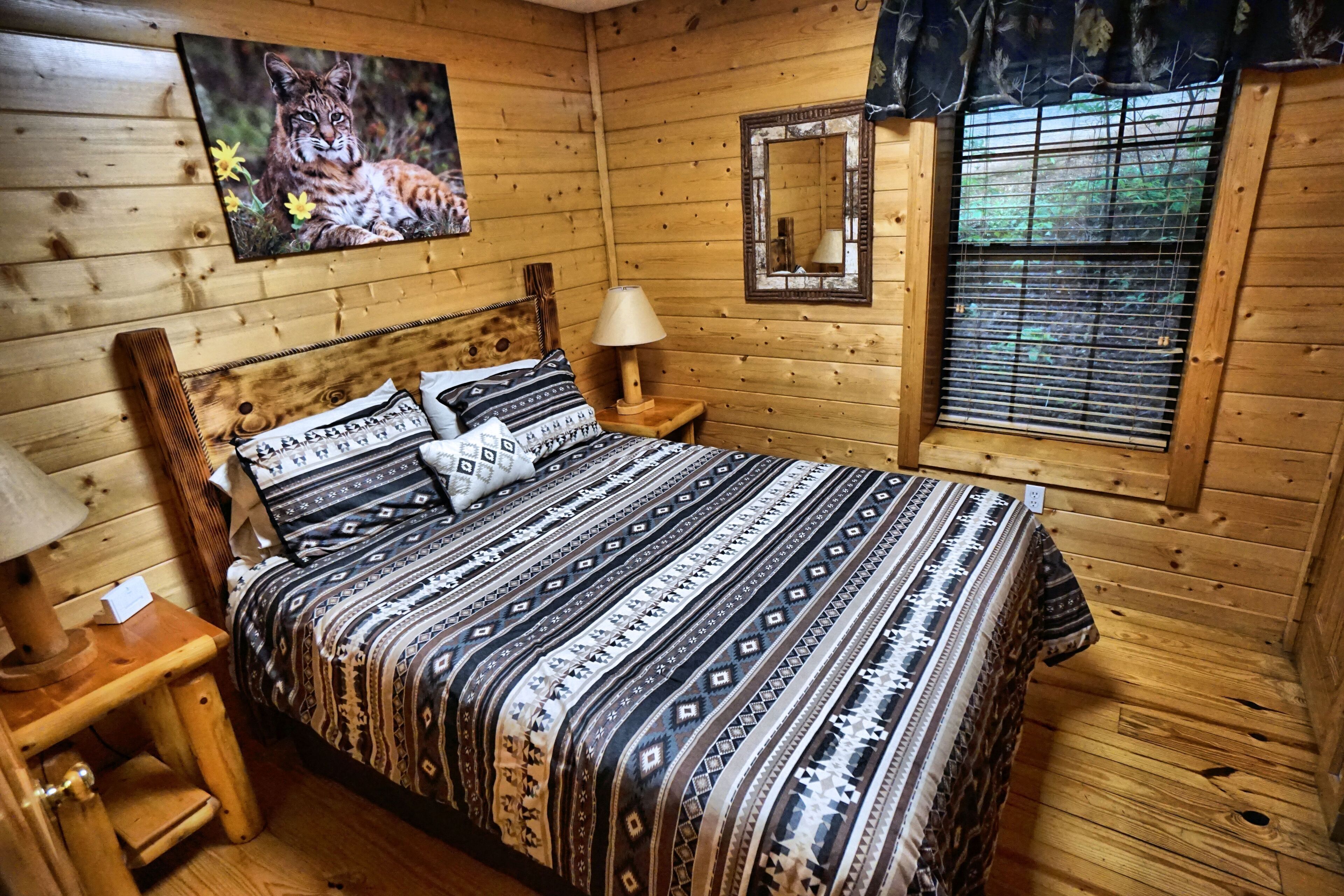 Ein Schlafzimmer einer Holzhütte mit Bett, Nachttisch, Lampe und einem Fenster mit Jalousien.