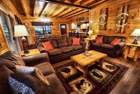A cozy log cabin interior with leather sofas, a wooden coffee table, and a dining area.