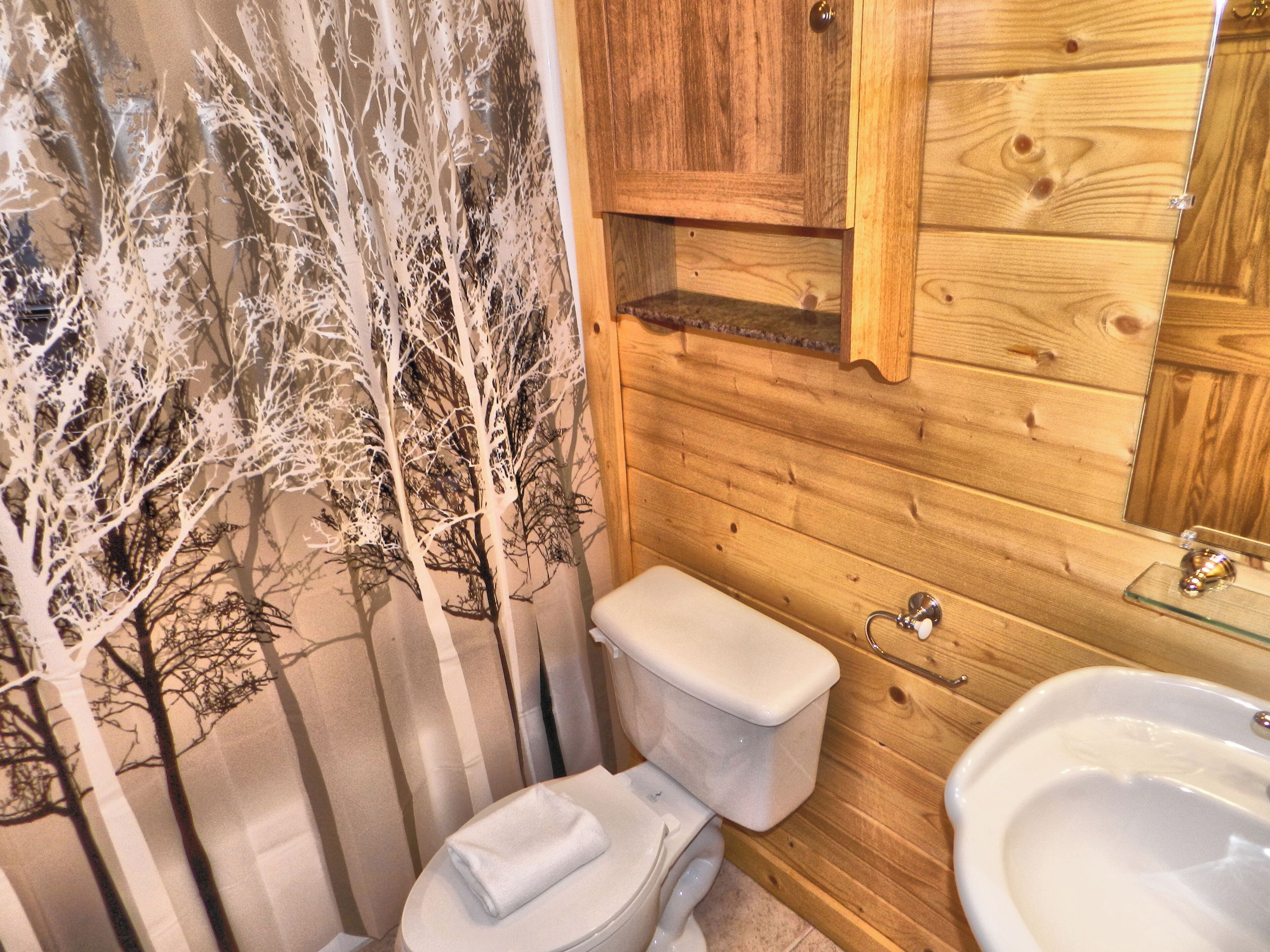Une salle de bain en bois comprenant des toilettes, un lavabo et une fresque murale représentant un arbre décoratif.