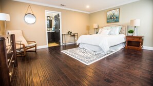A bedroom with a large bed, a chair, a dresser, a nightstand, and a painting on the wall.