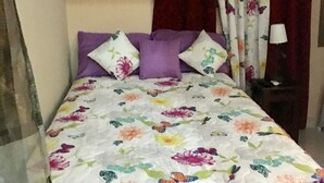A bed with a floral bedspread, purple pillows, and red curtains. - Maria Bonita, Locate Near The Center Of The Higuey City (Higüey)