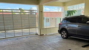 A covered parking area with a car, a concrete floor, and a view through the open garage door. - Maria Bonita, Locate Near The Center Of The Higuey City (Higüey)