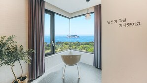 A modern room with a large window, a view of the sea, and a small table. - Jeju Bricks Hotel (Seogwipo)