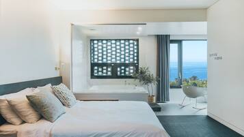A modern bedroom with a large bed, a bathtub, and a view of the ocean.
