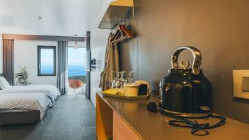 A hotel room with a bed, a desk with a kettle, a tray with cups, and a view of the sea.