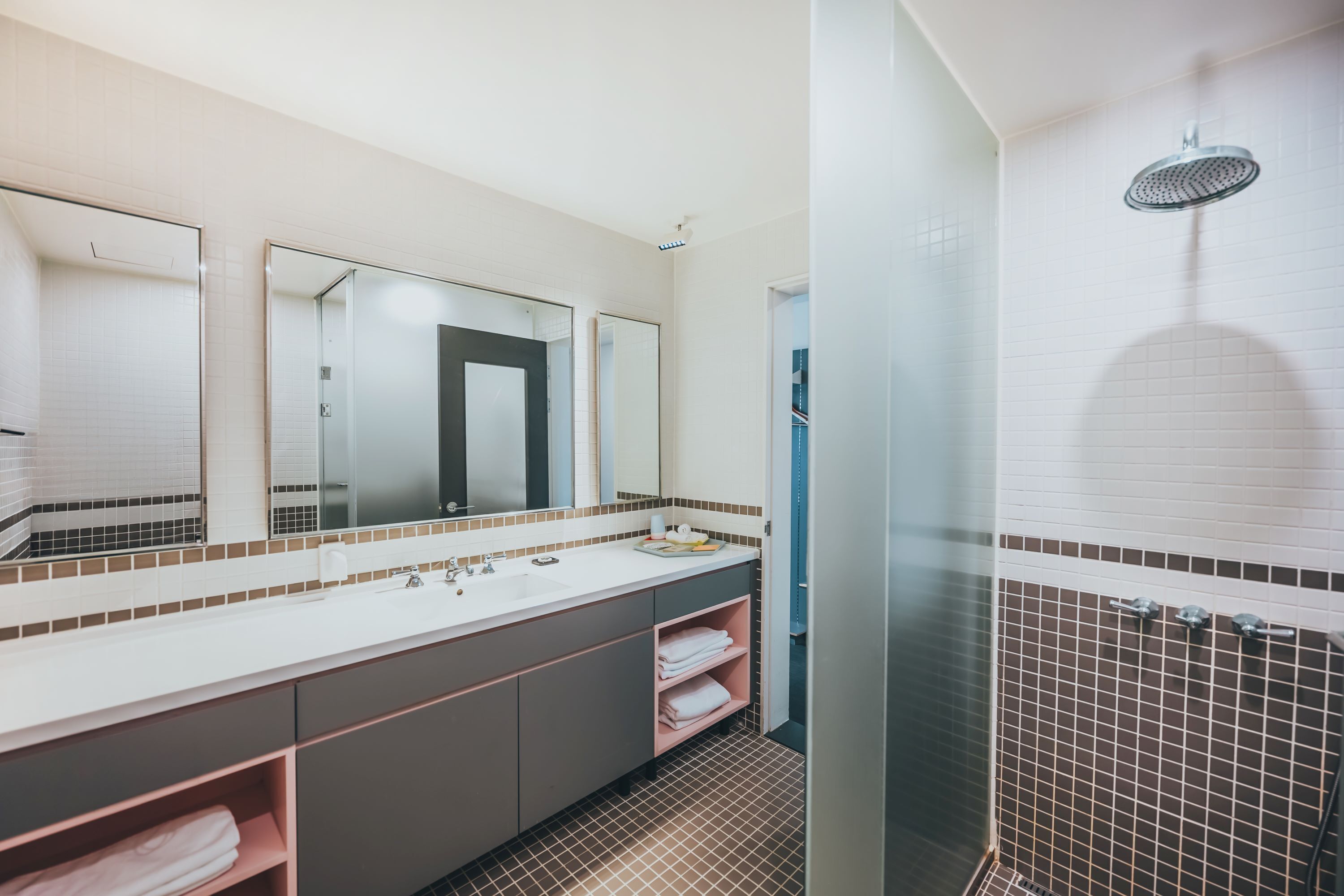 A modern bathroom with a large mirror, a shower, and a vanity with a sink and towel rack.
