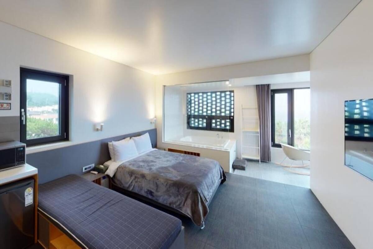 A modern hotel room with a bed, bedside table, desk, and a view of the outdoors.