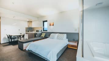 A modern bedroom with a bed, bedside tables, a desk, and a kitchenette.