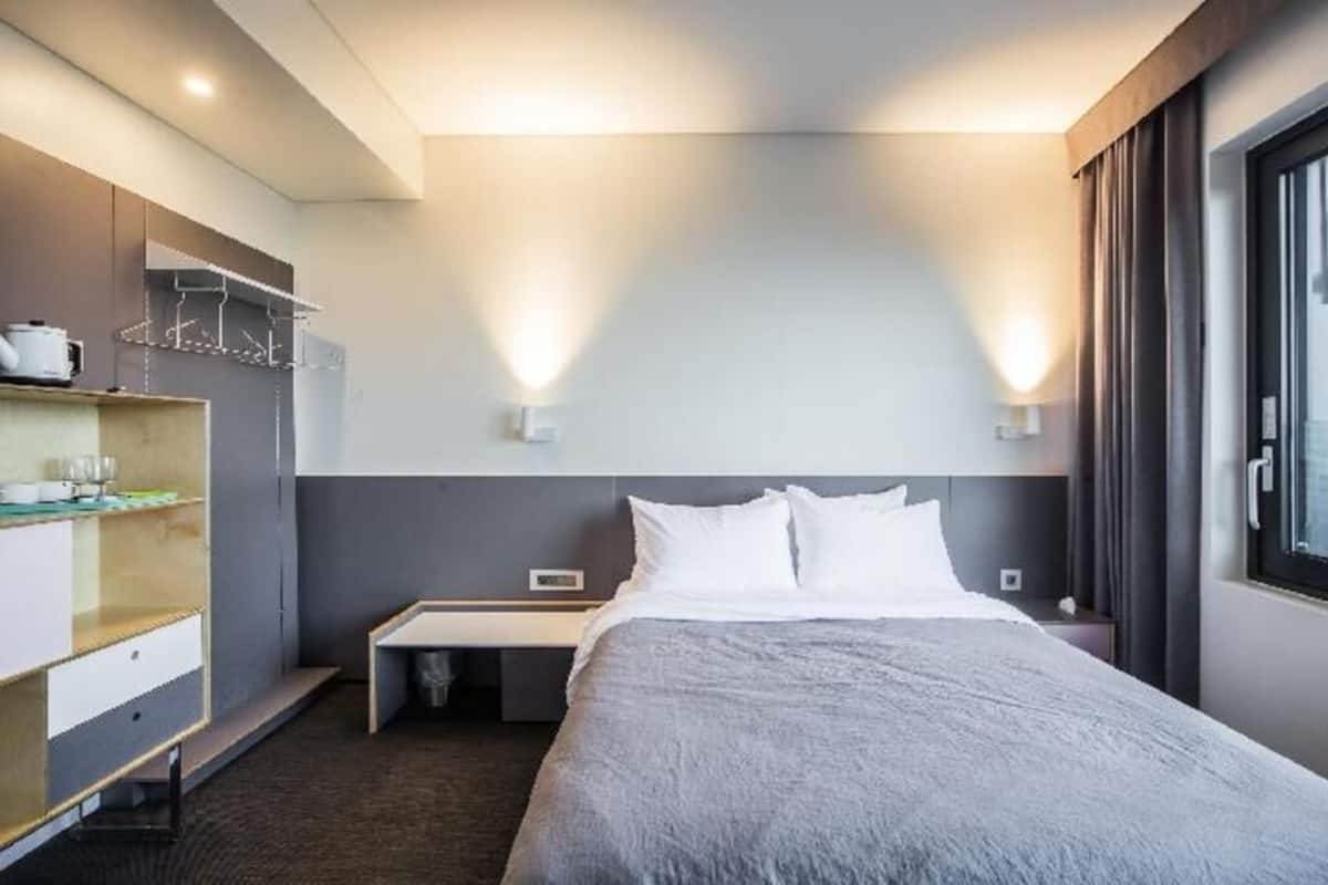 A hotel room with a bed, bedside table, and a desk with a chair.