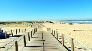 A wooden boardwalk leading to a sandy beach with dunes in the background.