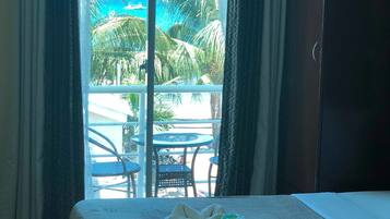 A hotel room with a bed, a wardrobe, and a view of a pool and palm trees.