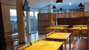A restaurant with wooden tables and benches, pendant lighting, a TV mounted on the wall, and a view of the sea through the windows. - S-E Hotel and Residence (Malay)