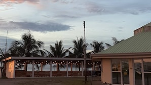 A beachside building with a covered seating area, palm trees, and a view of the ocean. - S-E Hotel and Residence (Malay)