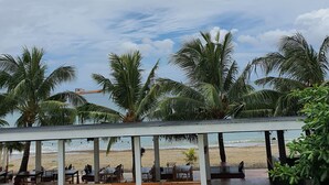 A beachside restaurant with outdoor seating, palm trees, and a view of the ocean. - S-E Hotel and Residence (Malay)