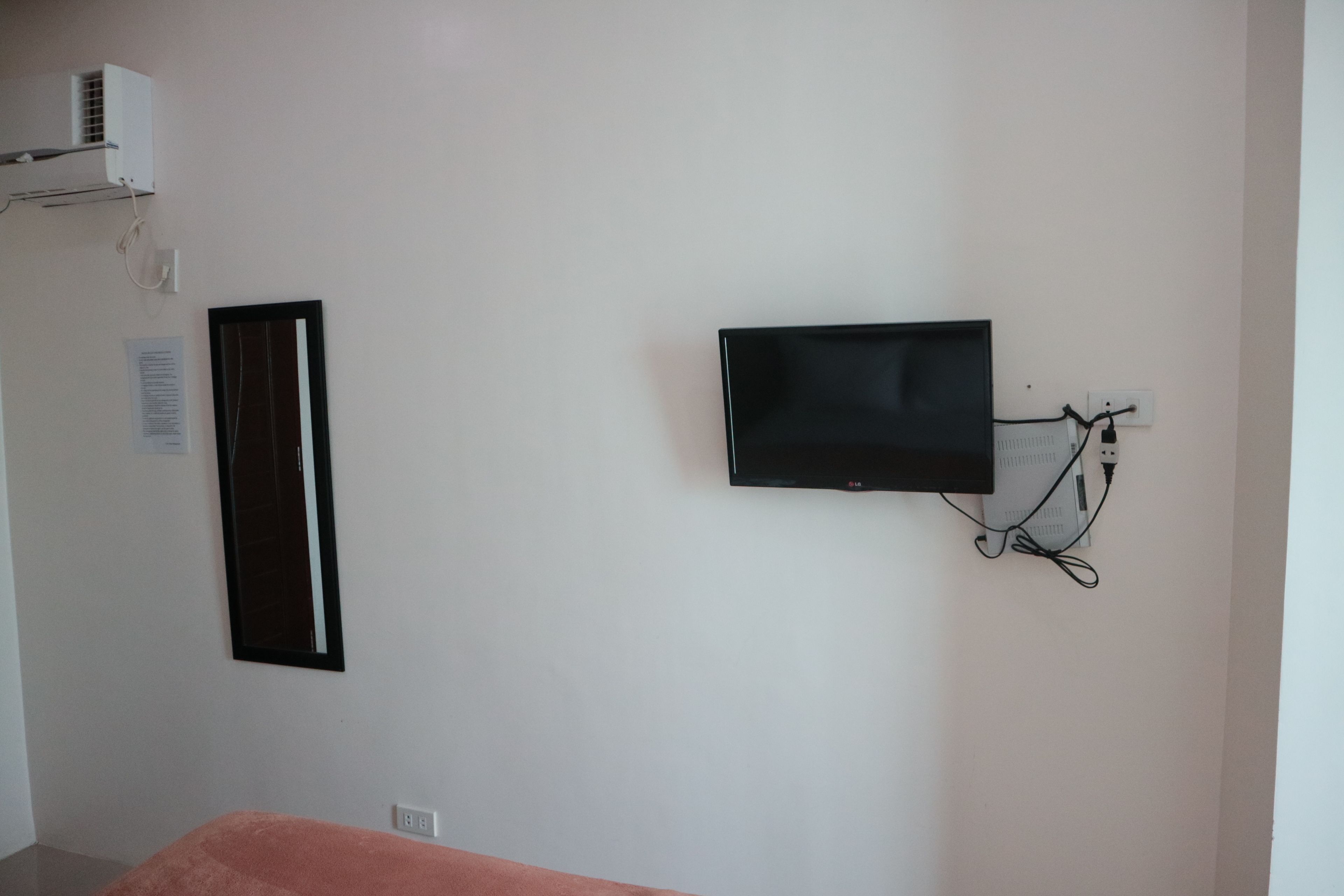 A room with a flat-screen TV mounted on the wall, a power outlet, and a white air conditioning unit.
