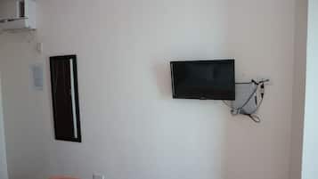 A room with a flat-screen TV mounted on the wall, a power outlet, and a white air conditioning unit.