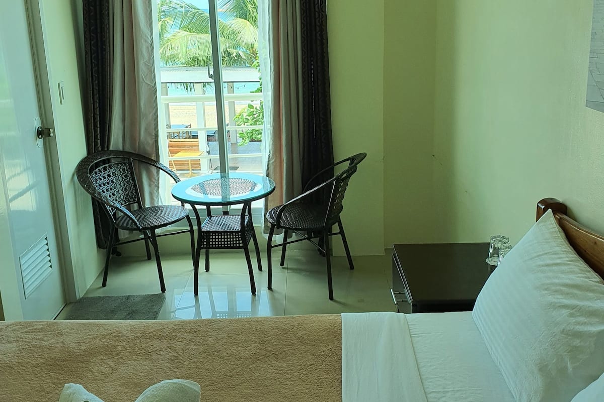 Una habitación de hotel con cama, una pequeña mesa con dos sillas y vistas al balcón exterior.