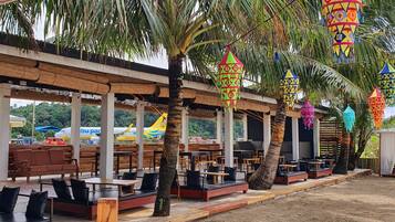 A wooden sign with "KAMs" and "Catlican" text, surrounded by outdoor seating and palm trees.