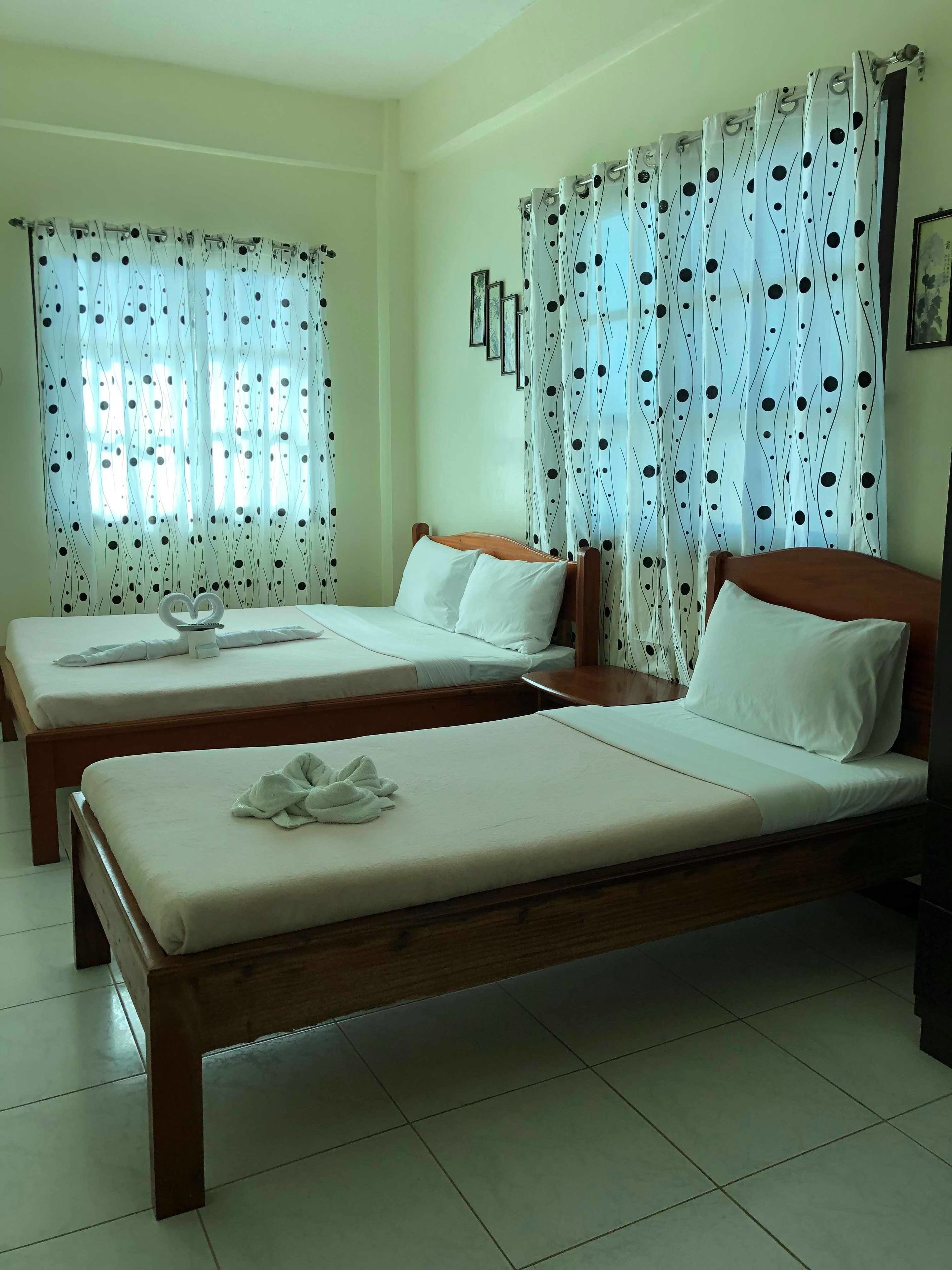 Habitación de hotel con dos camas individuales, cabecera de madera, ropa de cama blanca y un ventanal con cortinas estampadas.