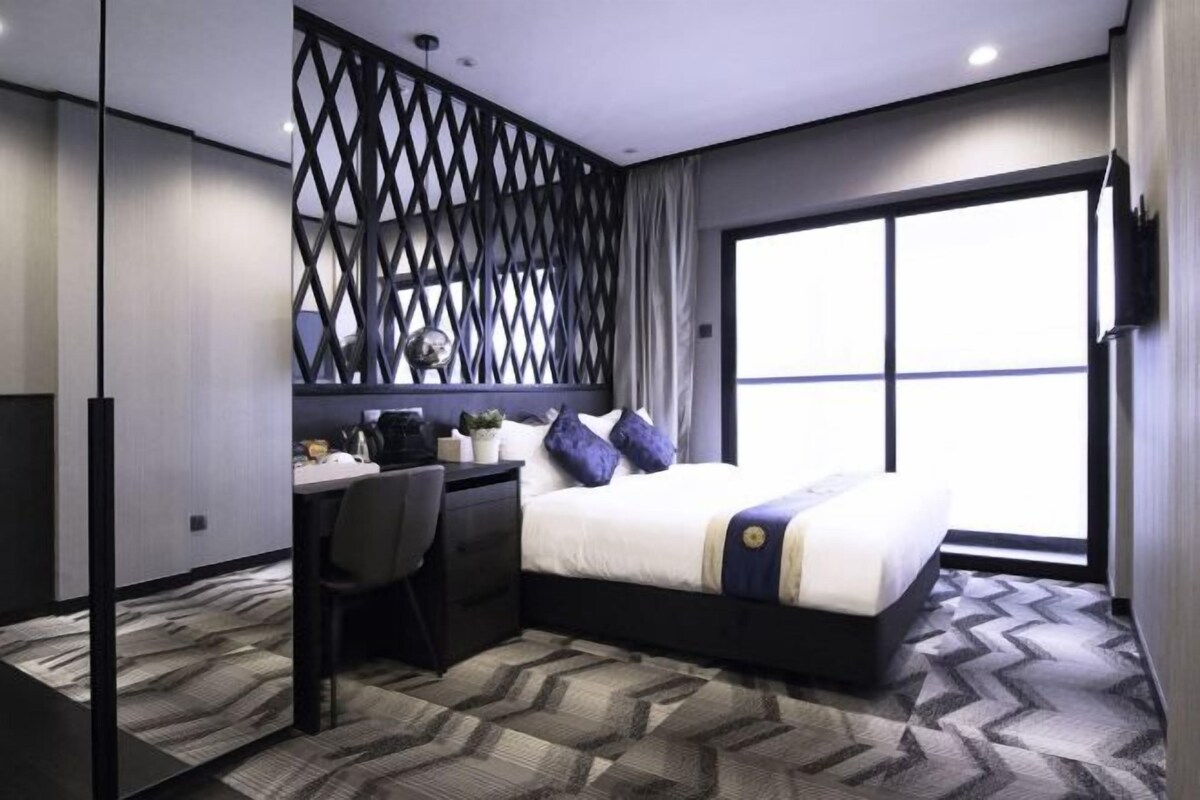 Une chambre d’hôtel moderne dotée d’un grand lit, d’un bureau avec une chaise, d’un mur décoratif et d’une grande fenêtre.