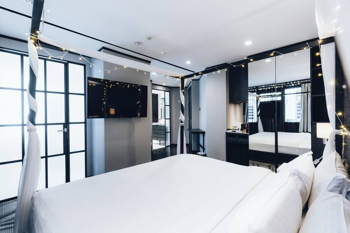 Une chambre d’hôtel moderne dotée d’un grand lit, d’un téléviseur fixé au mur et offrant une vue sur la ville grâce à de grandes fenêtres.