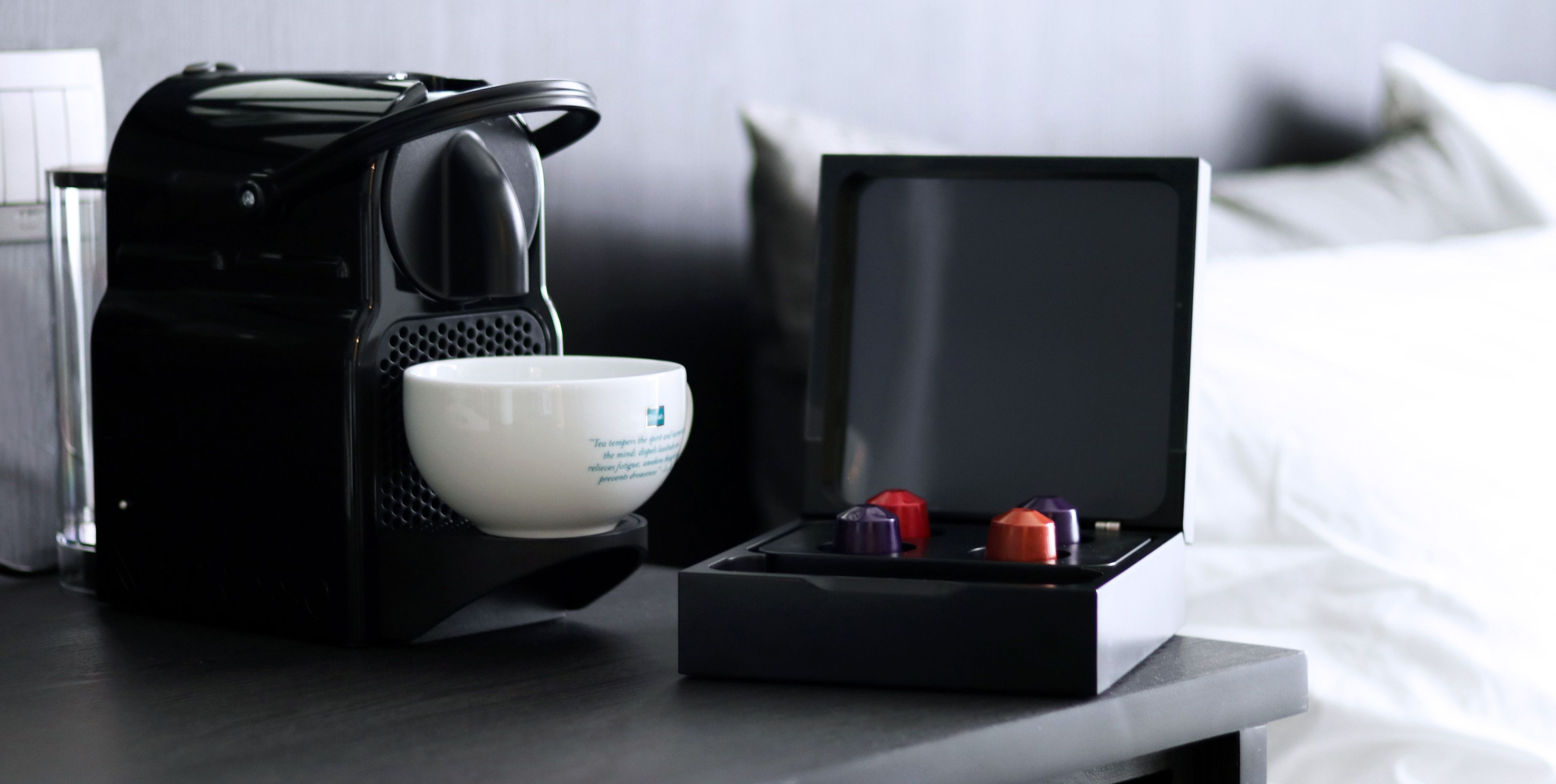 A coffee maker with a cup and a box of tea bags on a table.