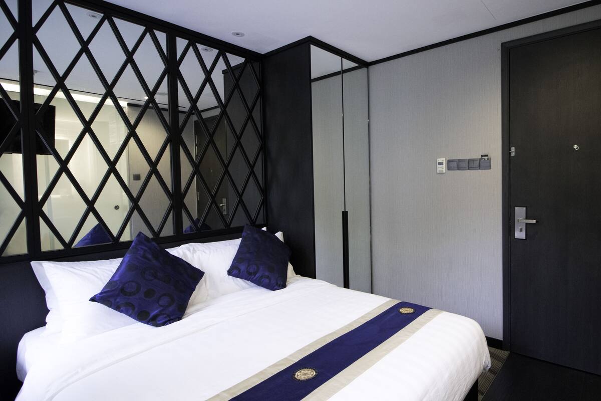 Une chambre d’hôtel avec un lit, une porte sombre et un mur orné d’un motif géométrique.