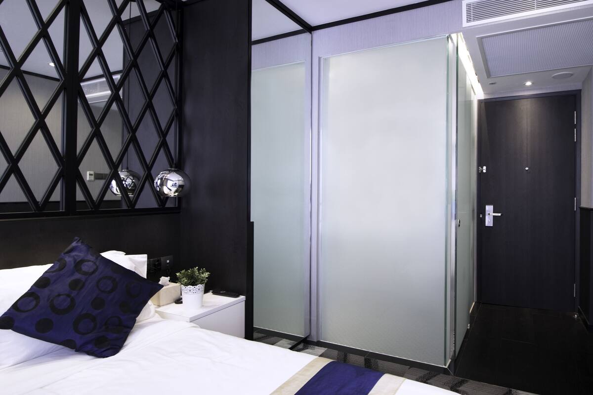 Une chambre d’hôtel avec un lit, une armoire, un miroir et une petite table sur laquelle est posée une plante.
