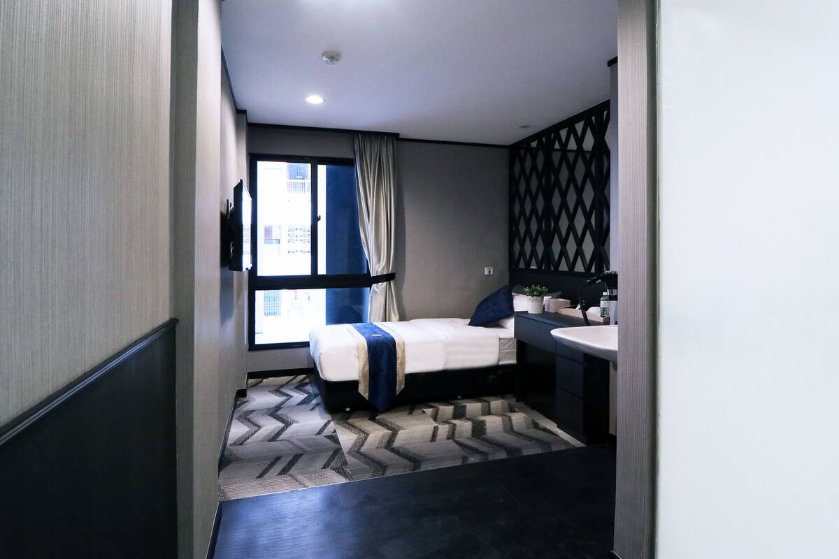 Une chambre d’hôtel moderne équipée d’un lit, d’un bureau, d’une chaise, d’une fenêtre avec des rideaux et d’une salle de bain avec un lavabo et un miroir.