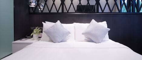 A modern bedroom with a large bed, two pillows, a nightstand with a lamp, and a potted plant.