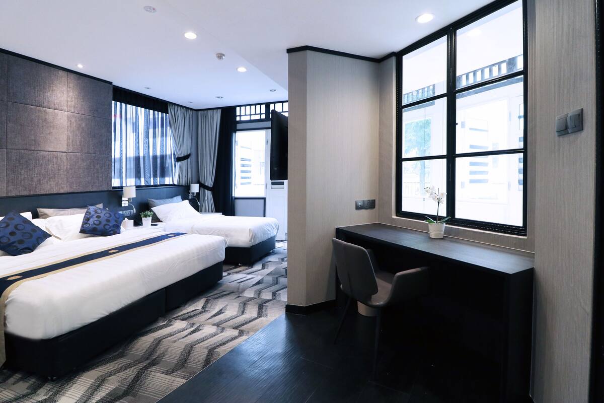Une chambre d’hôtel moderne avec deux lits, un bureau et de grandes fenêtres.