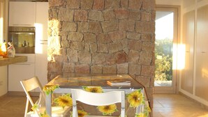 Un comedor con pared de piedra, una mesa, sillas y vistas a través de un ventanal.