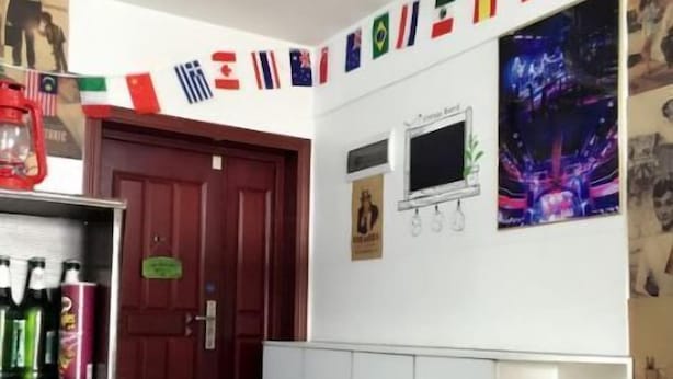 Et hotel lobby med en røddør, en receptionsdisk med vand på flaske, et tv-skærm og en væg dekoreret med diverse flag.