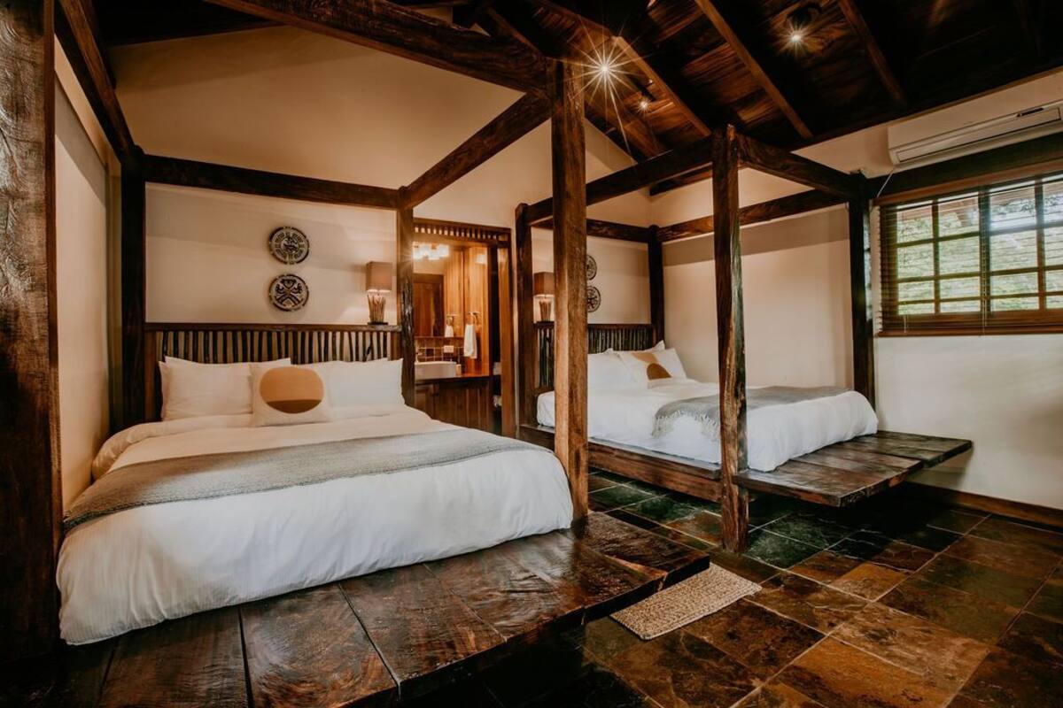 Una habitación tradicional con techo de madera y suelo de piedra, que incluye dos camas y una pequeña mesa.