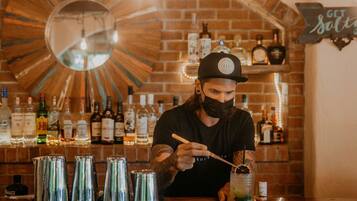 A bartender preparing a drink at a bar with a brick wall and various bottles in the background.