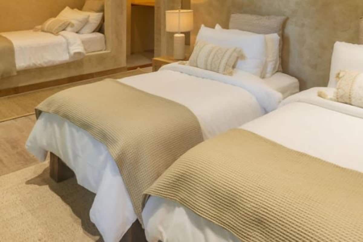 Una habitación de hotel con una cama grande, una cama más pequeña, un ventilador de techo y un espejo sobre la cama más pequeña.