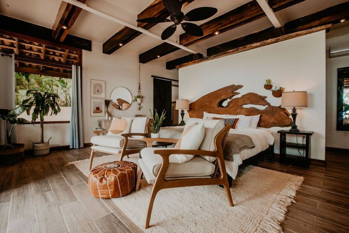 Un dormitorio con una cama grande, vigas de madera en el techo y vistas a la vegetación exterior.
