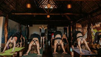 A yoga class in a rustic room with wooden beams and a thatched roof.