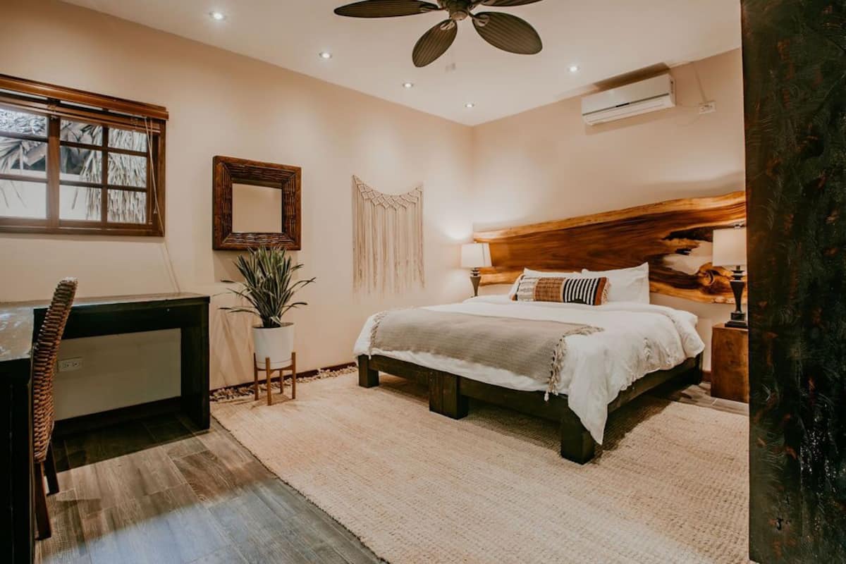 Un dormitorio con cama, escritorio, silla, ventilador de techo y ventana con persianas.