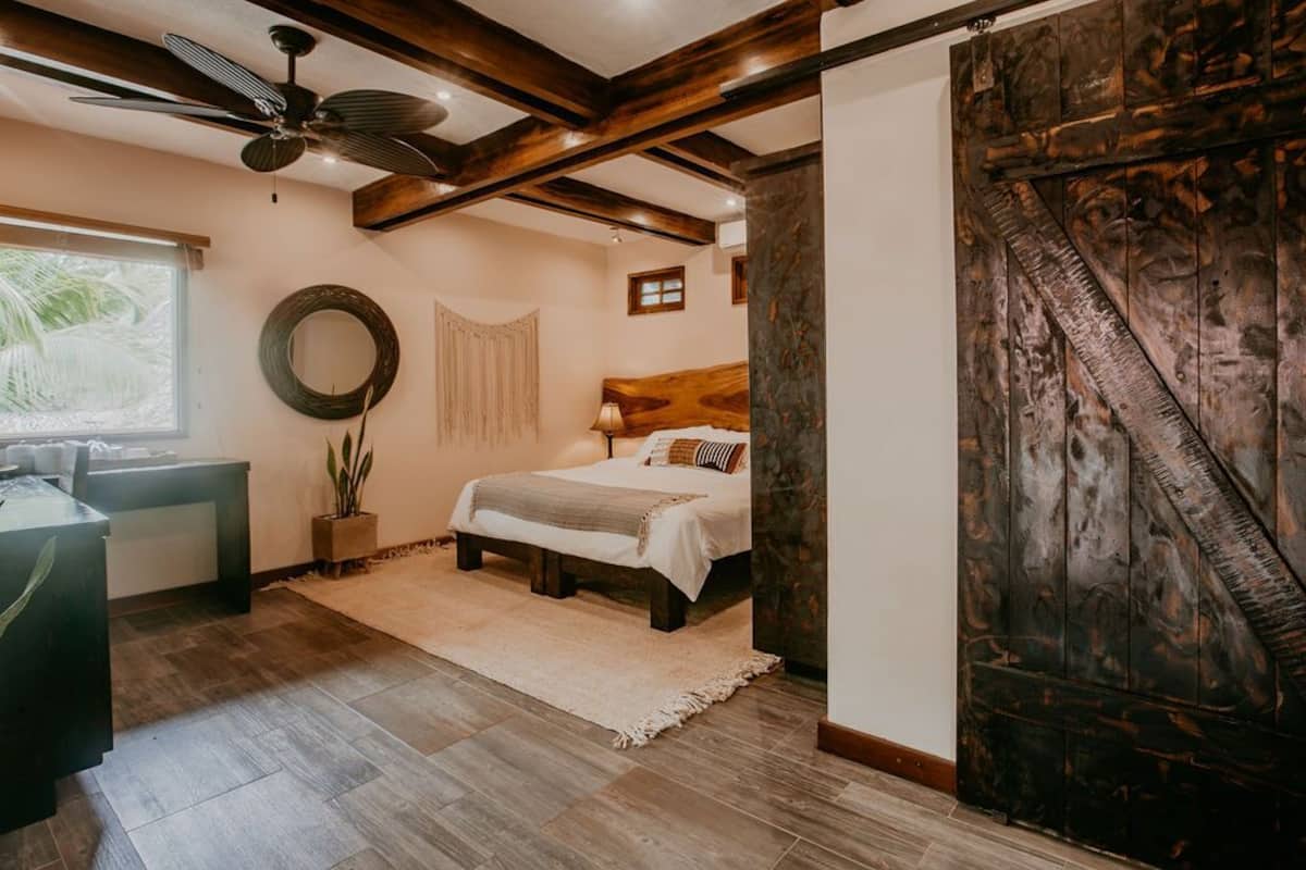 Un dormitorio con cama, escritorio, ventilador de techo y una puerta grande de madera.