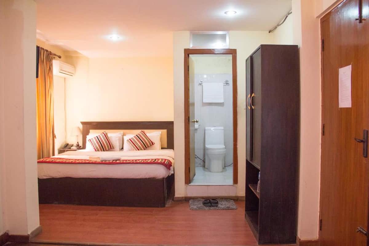 A compact hotel room with a single bed, a wardrobe, a small bathroom with a toilet and a mirror, and a door leading to another room.