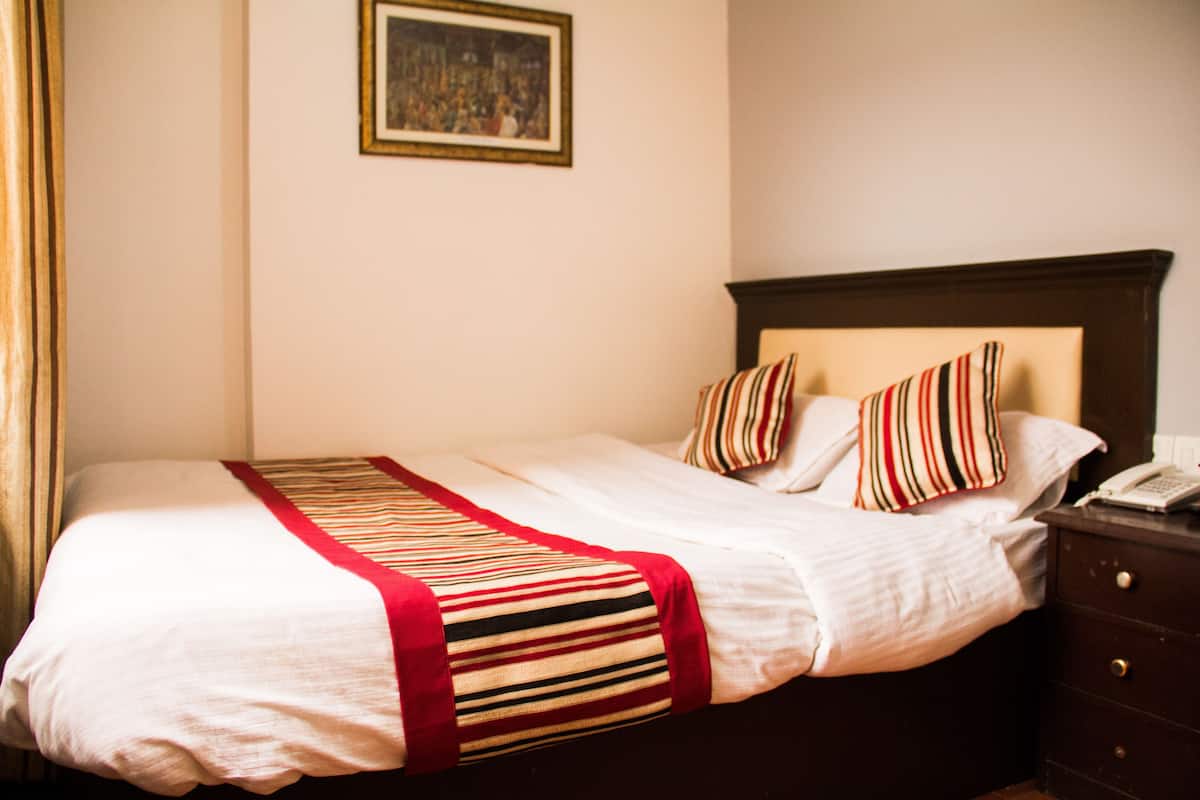 A neatly made bed with striped bedding and pillows, a wooden nightstand with a telephone, and a framed picture on the wall.