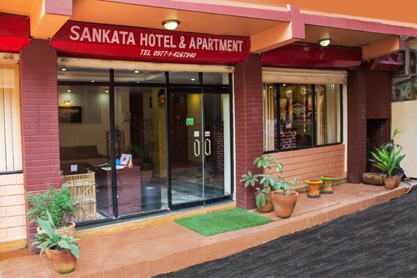 Exterior del Hotel & Apartamentos Sankata, con entrada de cristal, plantas en macetas y un felpudo verde en la entrada.