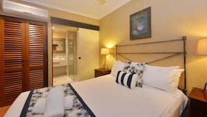 A hotel room with a bed, a ceiling fan, a nightstand, a lamp, and a painting on the wall.